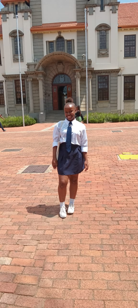 Amahle Jemane standing outside the University of Free State (UFS) main building, proudly wearing her high school uniform.